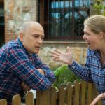 Egy nő és egy férfi vitatkozik a kerítés mellett, a nő dühösen gesztikulál.