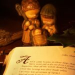 Karácsonyi jelenet, gyertya fényénél, betlehemi figurákkal és Bibliával.