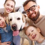 Egy boldog család kutyával, mosolygó gyerekek és szülők egy közeli fotón.