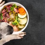 Egy kutya néz egy tál egészséges ételt, tele zöldségekkel és húsokkal.