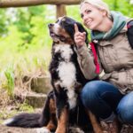 Egy nő és egy kutya pihennek a természetben, a nő mosolyogva mutat az égre.