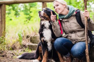 Egy nő és egy kutya pihennek a természetben, a nő mosolyogva mutat az égre.