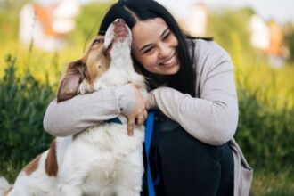 Egy nő boldogan öleli kutyáját, miközben a szabadban ülnek.