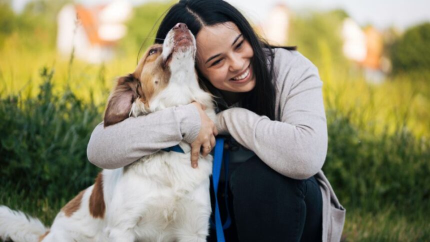 Egy nő boldogan öleli kutyáját, miközben a szabadban ülnek.