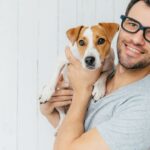 Egy férfi boldogan tart a karjában egy kutyát, mosolyogva néz a kamerába.