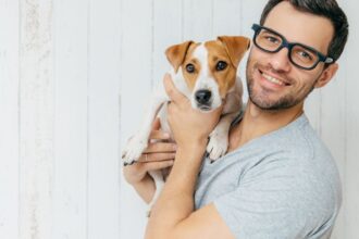 Egy férfi boldogan tart a karjában egy kutyát, mosolyogva néz a kamerába.