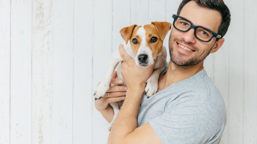 Egy férfi boldogan tart a karjában egy kutyát, mosolyogva néz a kamerába.